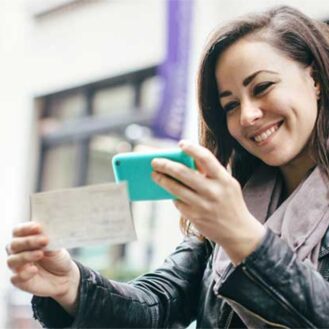 Girl using remote deposit with a check in one hand and her mobile phone in the other hand