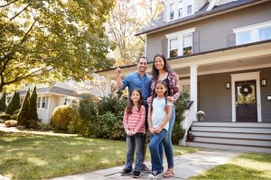 Family of four smiling in front of their new home in the Hudson Valley, holding house keys